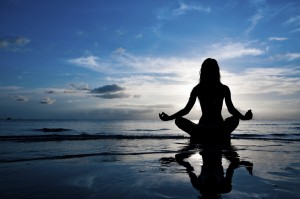 Woman in lotus position on shore at sunset