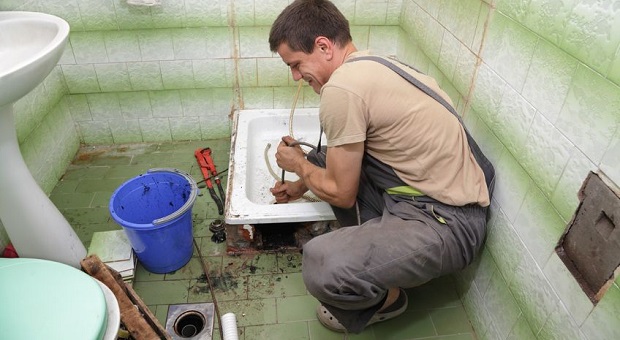 Plumber cleaning drain in bathroom with cable